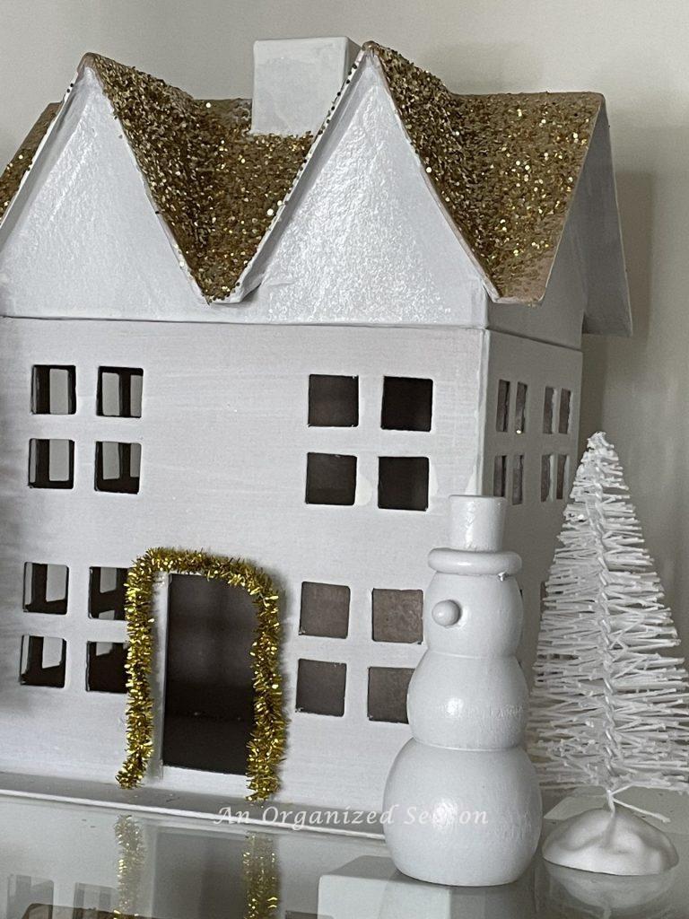 Wooden snowman in front of a white house in a styled Christmas village.