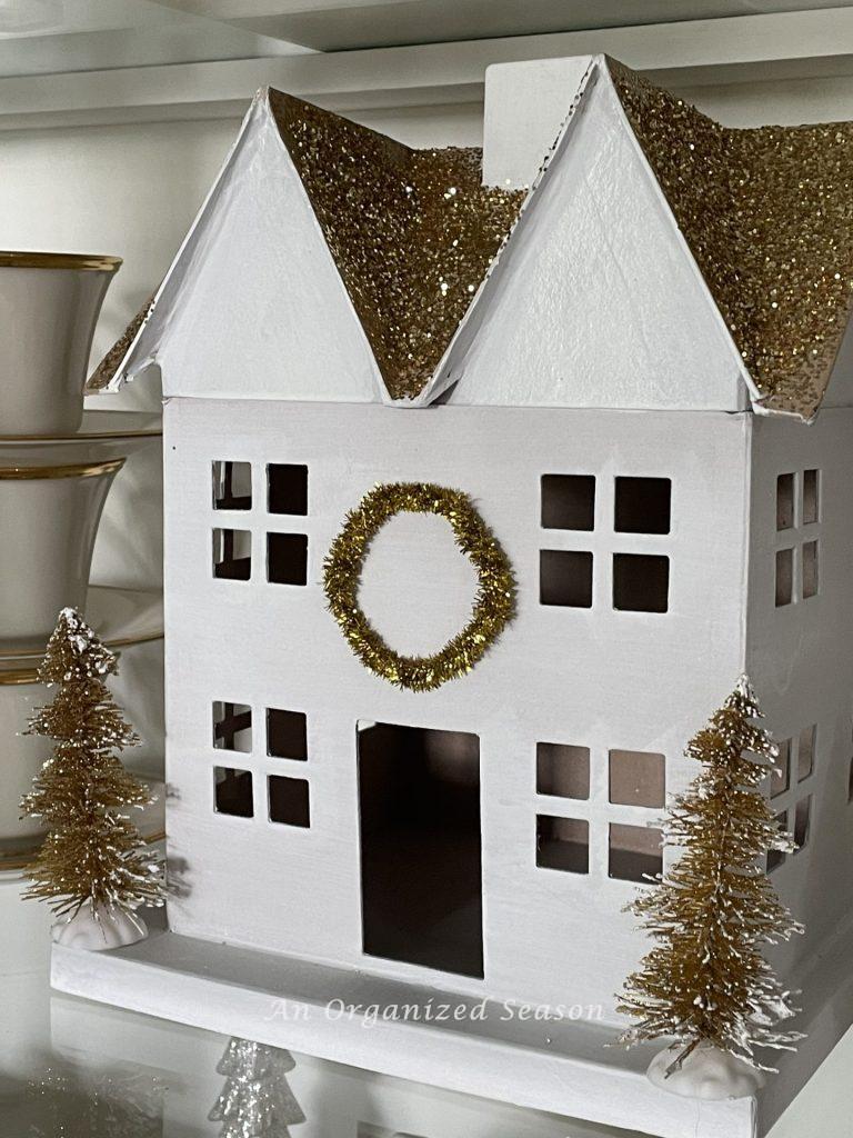 White house with gold glitter roof and a gold wreath with two gold bottle brush trees on each side. 