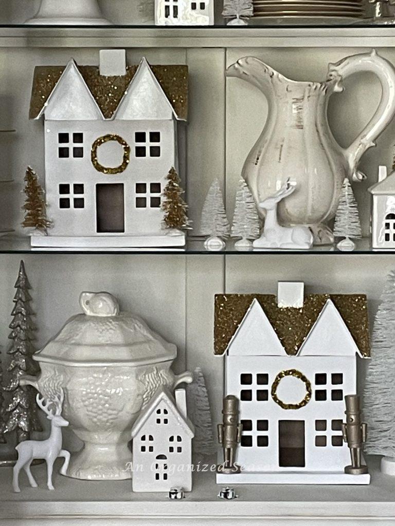 Christmas village white houses styled around white dishes in a china cabinet.  