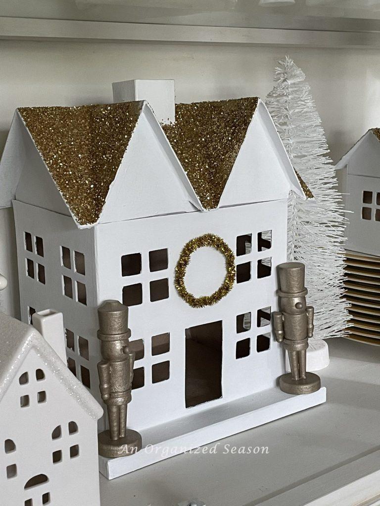 White house in a Christmas village styled with gold nutcrackers on each side of front door. 
