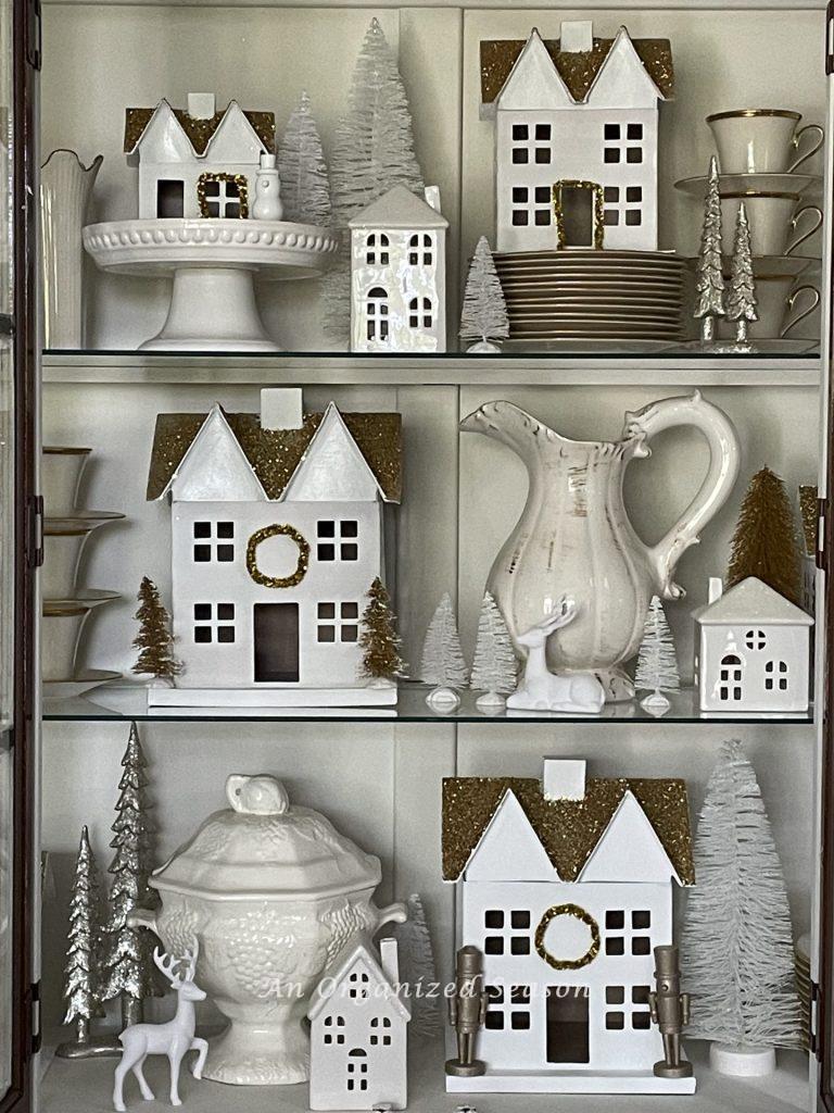 Christmas village with different height white houses styled in a china cabinet.  