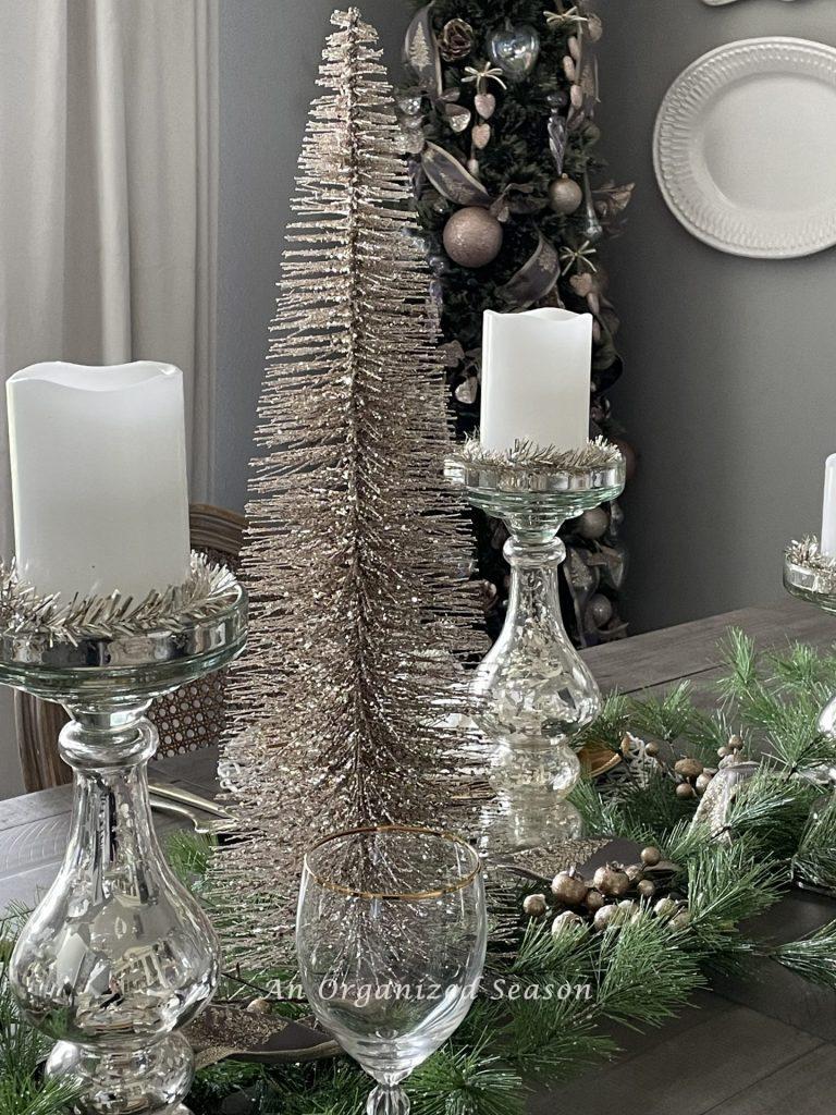 A tall pink bottlebrush Christmas tree and mercury glass candleholders decorate a dining room table. 