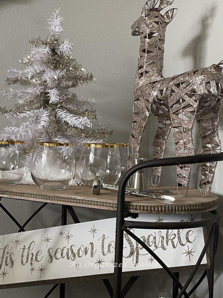 A dining room bar cart decorated for Christmas with a tinsel tree and pink reindeer.  