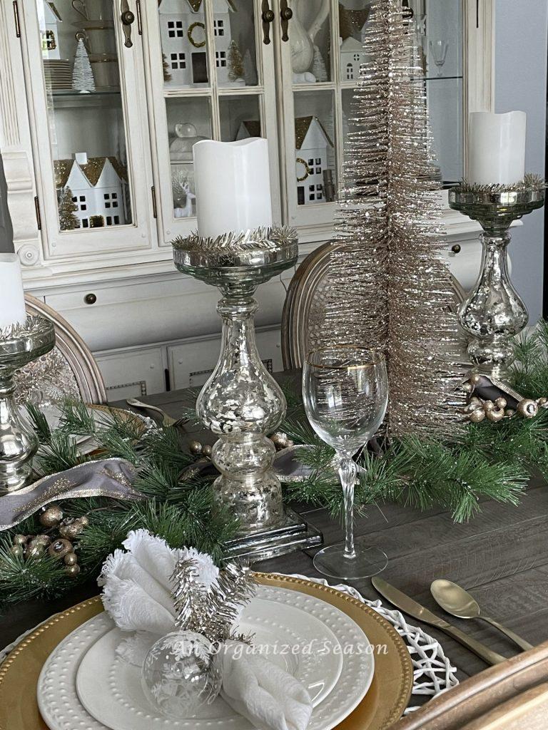 A dining room table decorated for Christmas with mercury glass candleholders and a pink bottlebrush tree, 