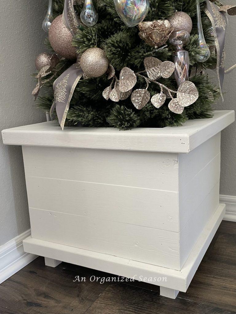 A white wooden tree collar holds a Christmas tree in a dining room. 