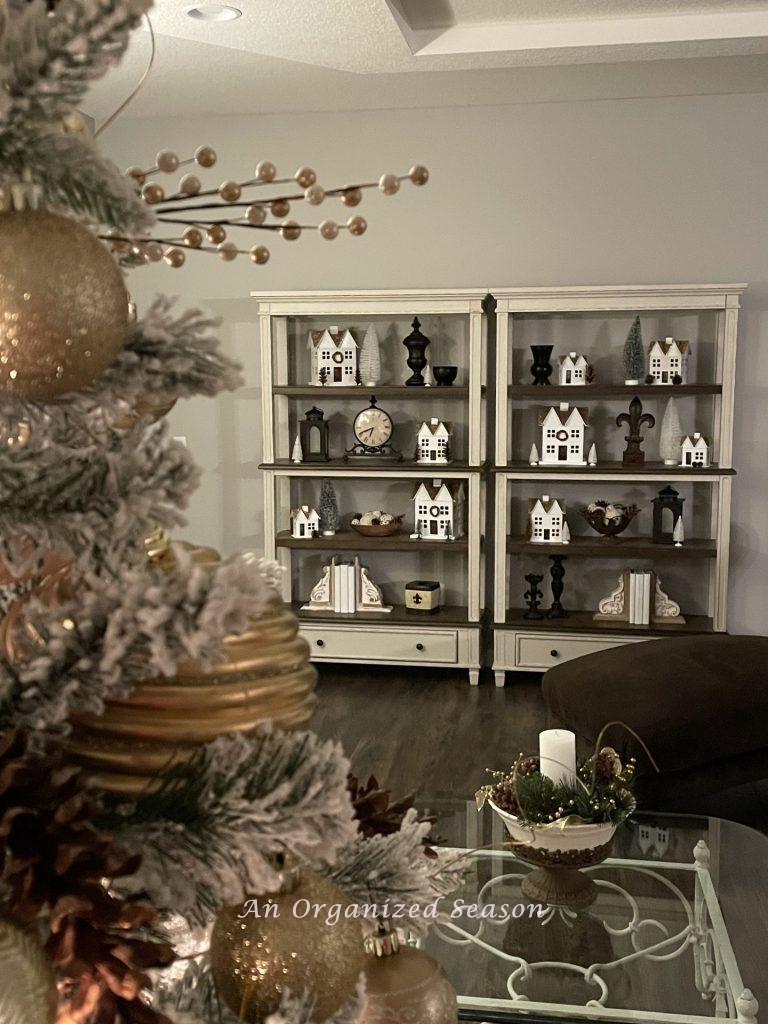 A white Christmas village styled on two bookshelves in a living room. 
