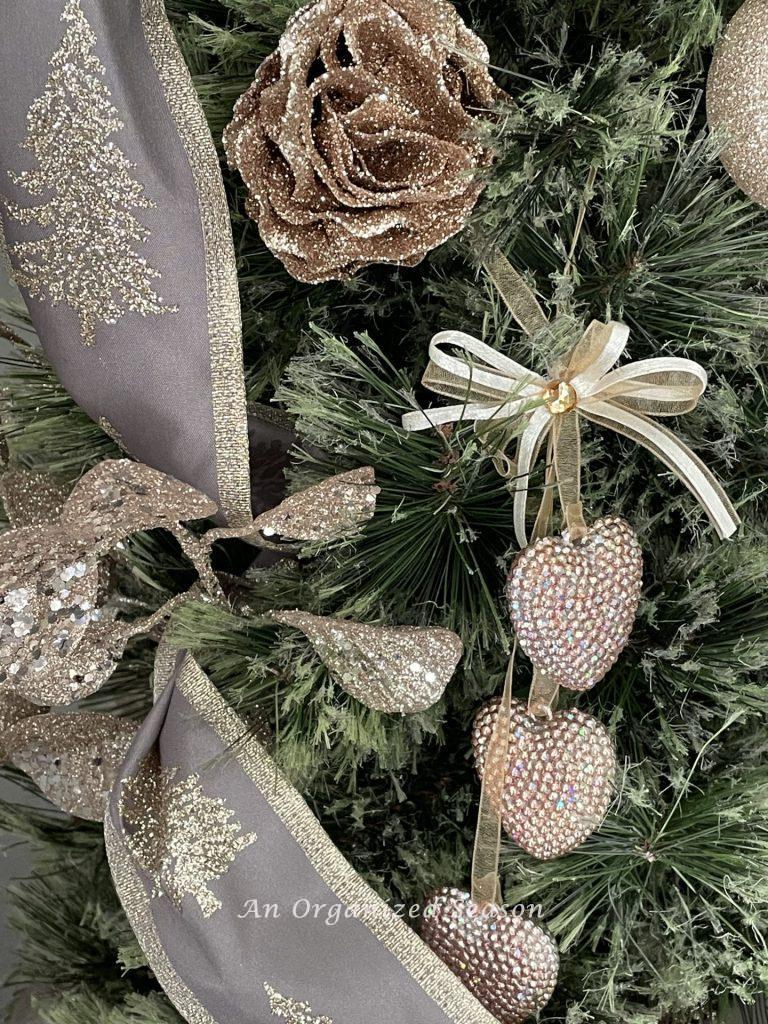 Pink glitter rose and a sparkly heart ornament hanging on a Christmas tree. 