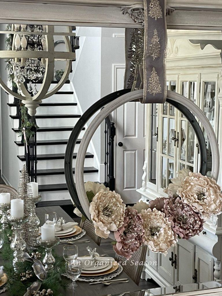 A wreath made with pink and white flowers hanging on a mirror in a dining room. 