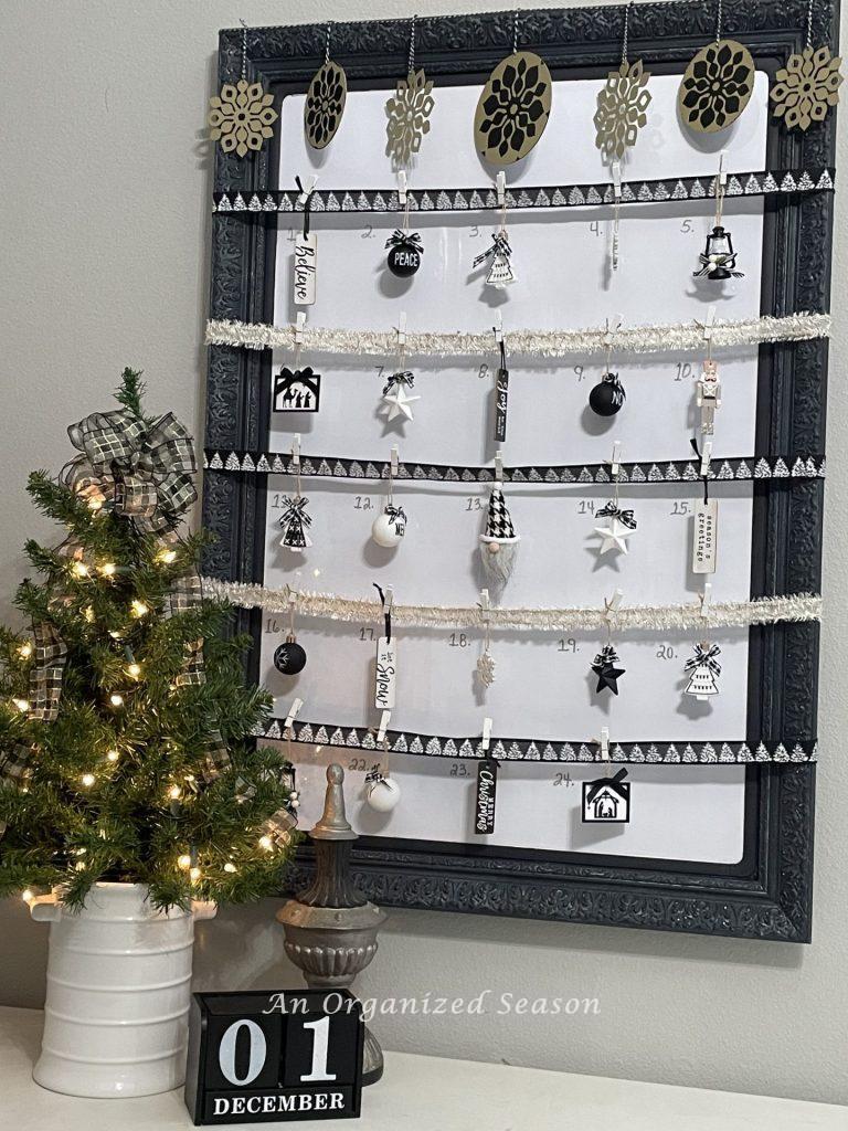 A DIY Advent calendar made with a framed white board, ribbon, and black and white Christmas ornaments.  