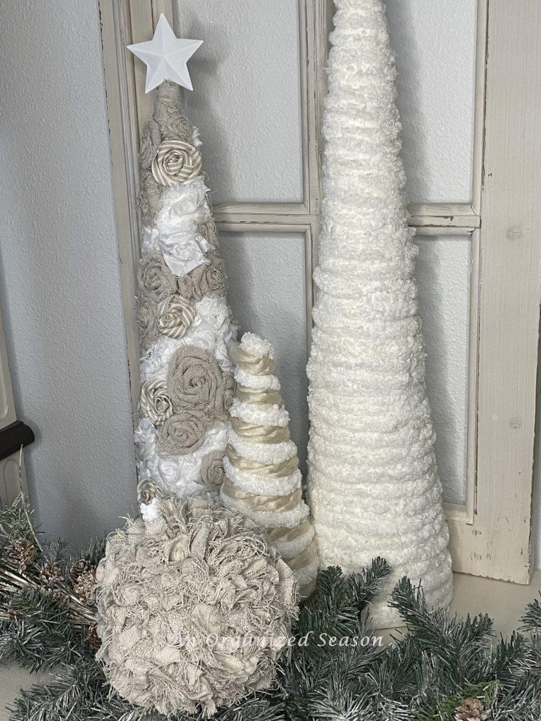 A vintage drop cloth Christmas ornament in front of three cone trees.