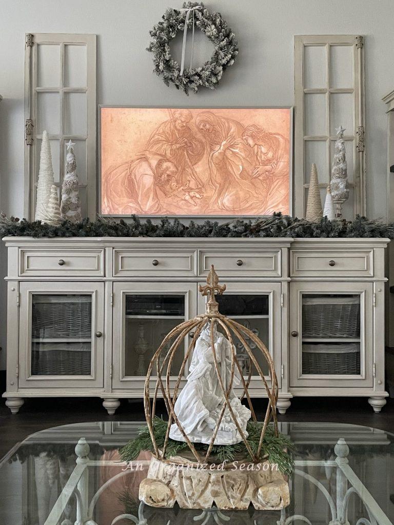 A cream console table with a picture frame tv hanging above it, displaying the Holy Family! 