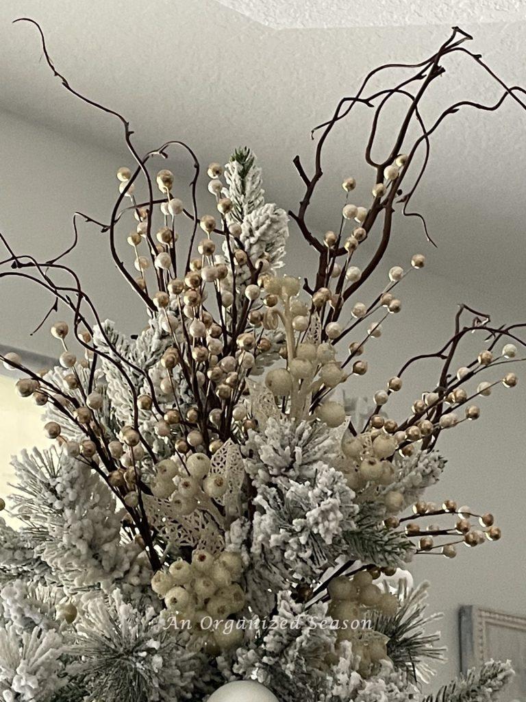 A Christmas tree topper made from tree branches, white berries, and champagne and white floral picks.