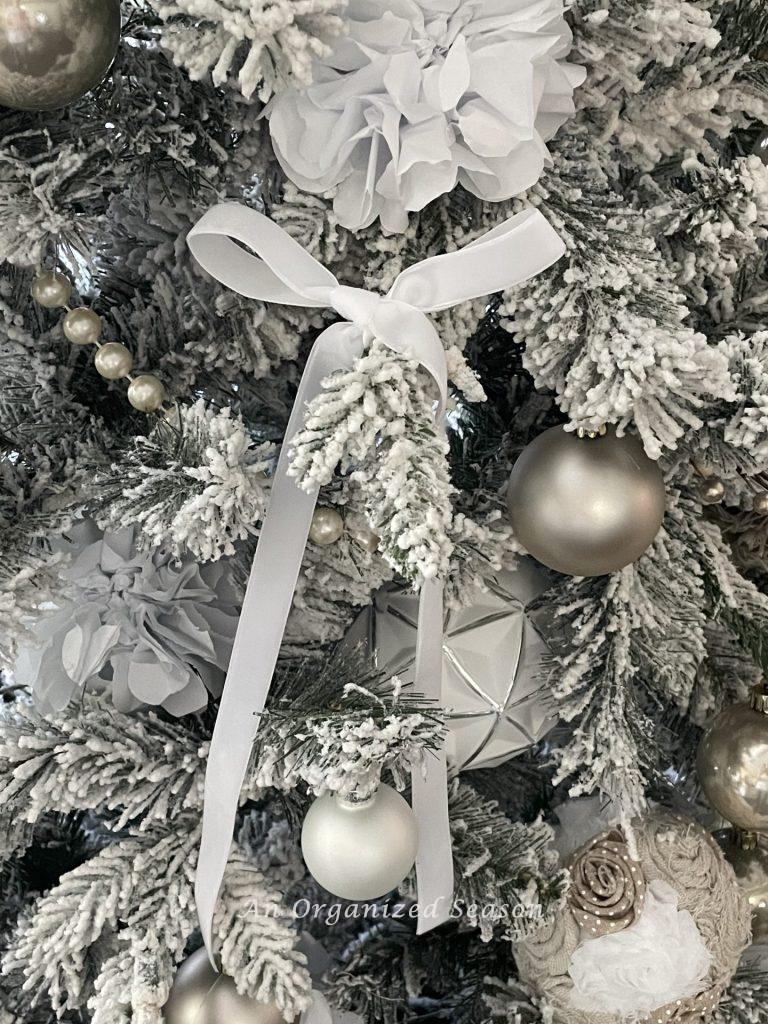 A white velvet bow hanging on a Christmas tree branch. 