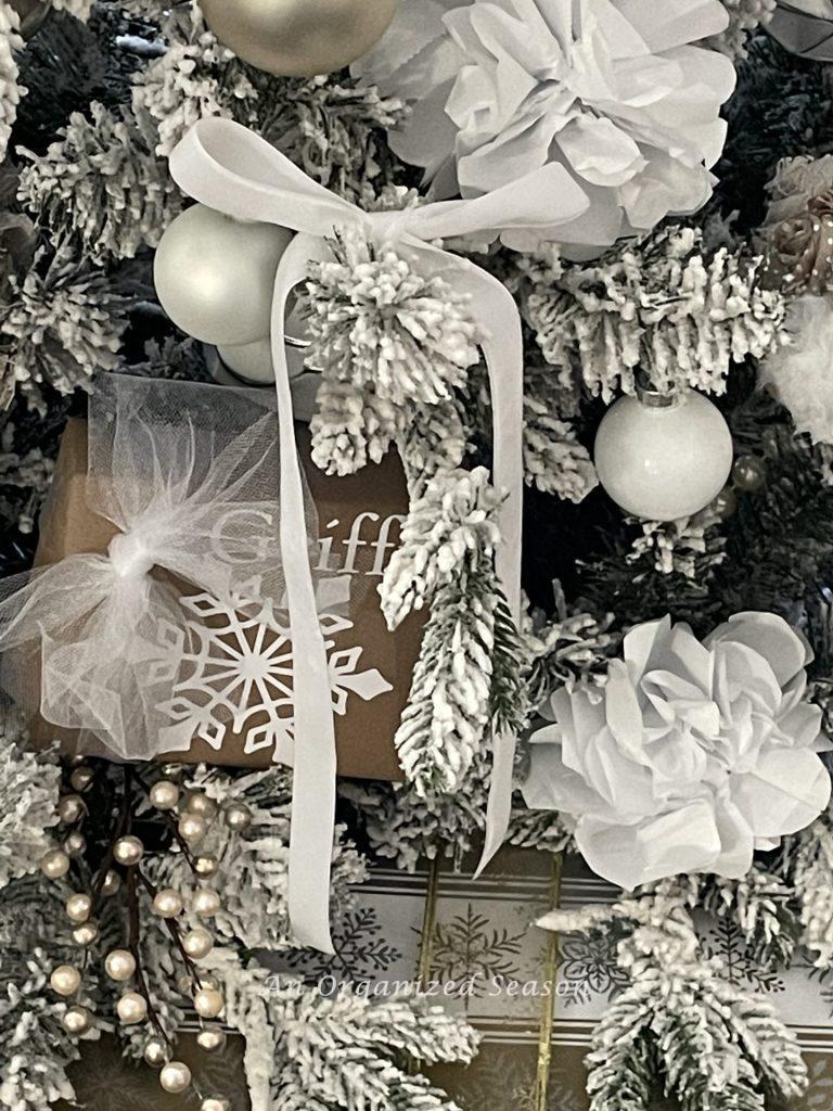 A Christmas tree with white paper flowers, white velvet bows,  and small wrapped packages. 