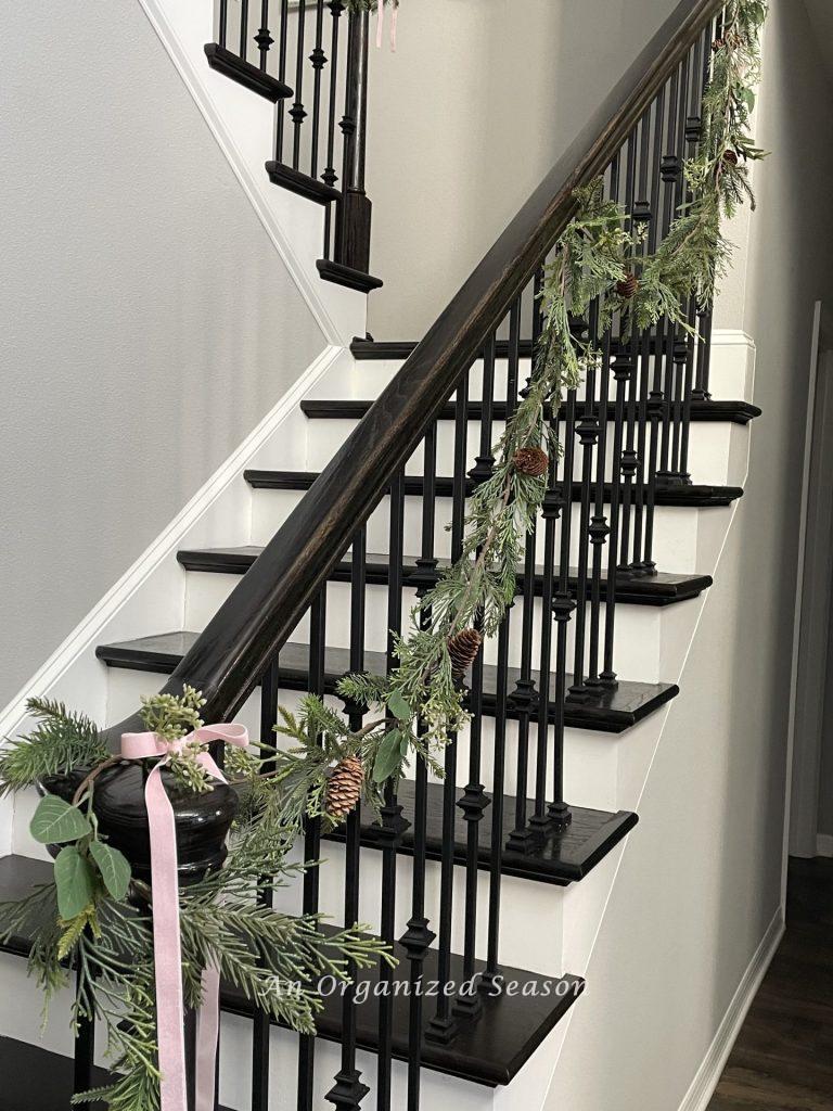 An evergreen and eucalyptus garland hanging on a staircase, is a good way to decorate for Christmas on a budget.