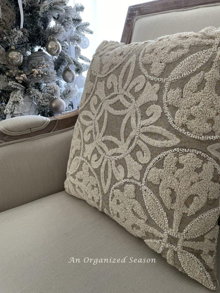 An embroidered pillow cover in cream, white, and champagne.