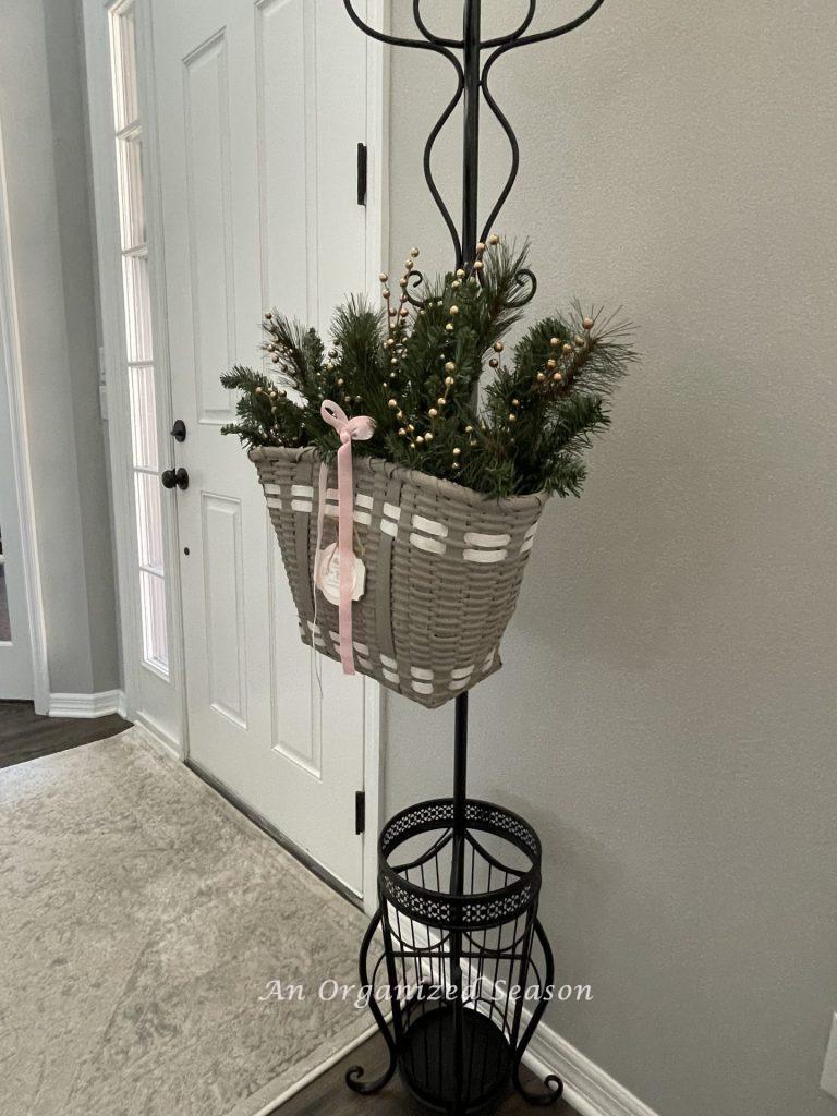 A gray basket holding evergreen branches with a pink velvet ribbon is a good way to decorate for Christmas on a budget.