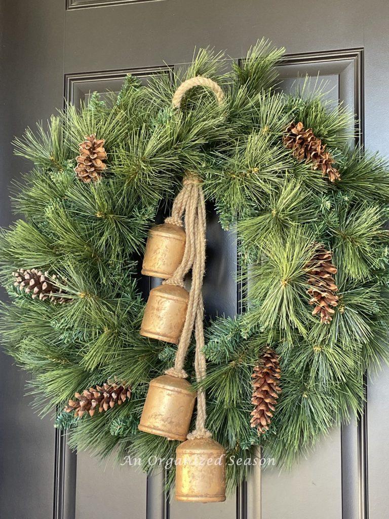 An evergreen wreath decorated with pine cones and antique bells is a good way to decorate for Christmas on a budget.