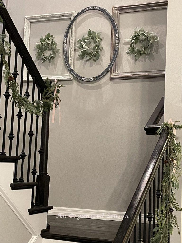 Three empty picture frames hanging on a wall with a wreath inside each one,  is a good way to decorate for Christmas on a budget.