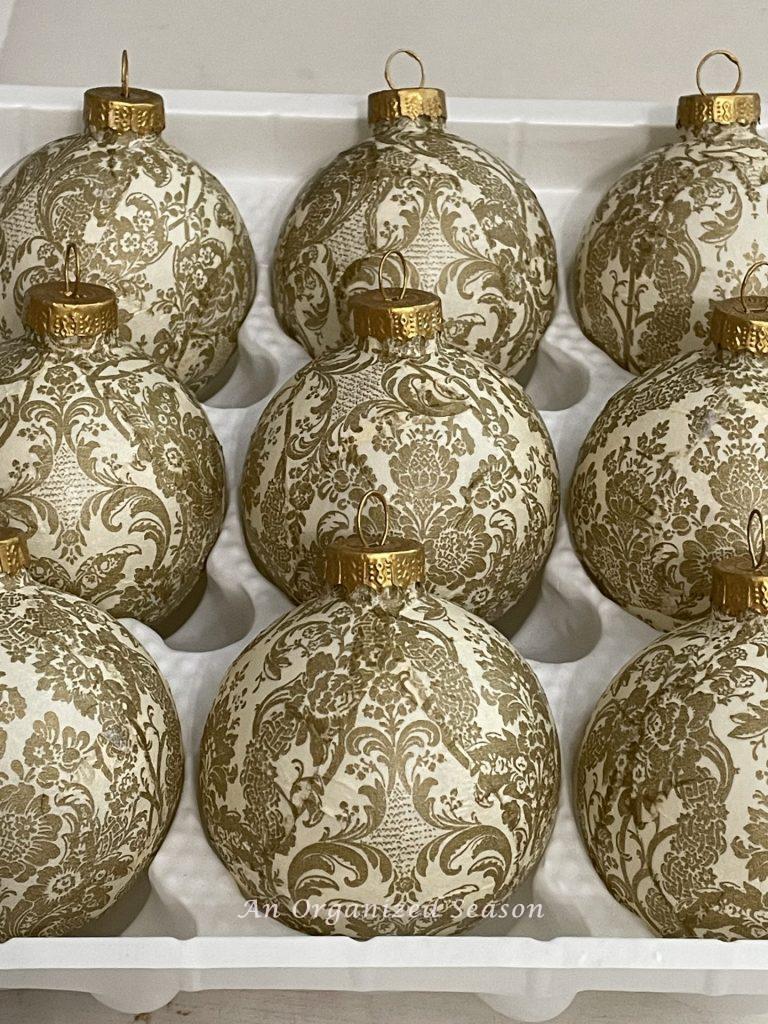 A tray of decoupaged Christmas ornaments made with gold and cream napkins. 