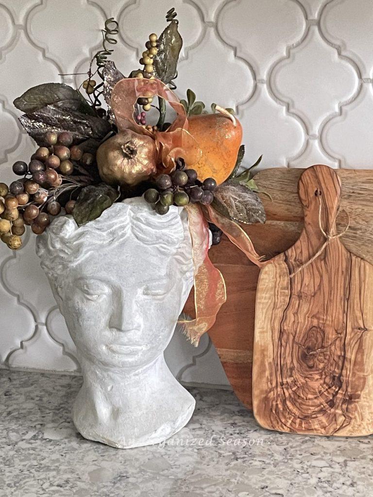 Two cutting boards and a bust planter filled with fruit decorate a kitchen counter for Christmas. 