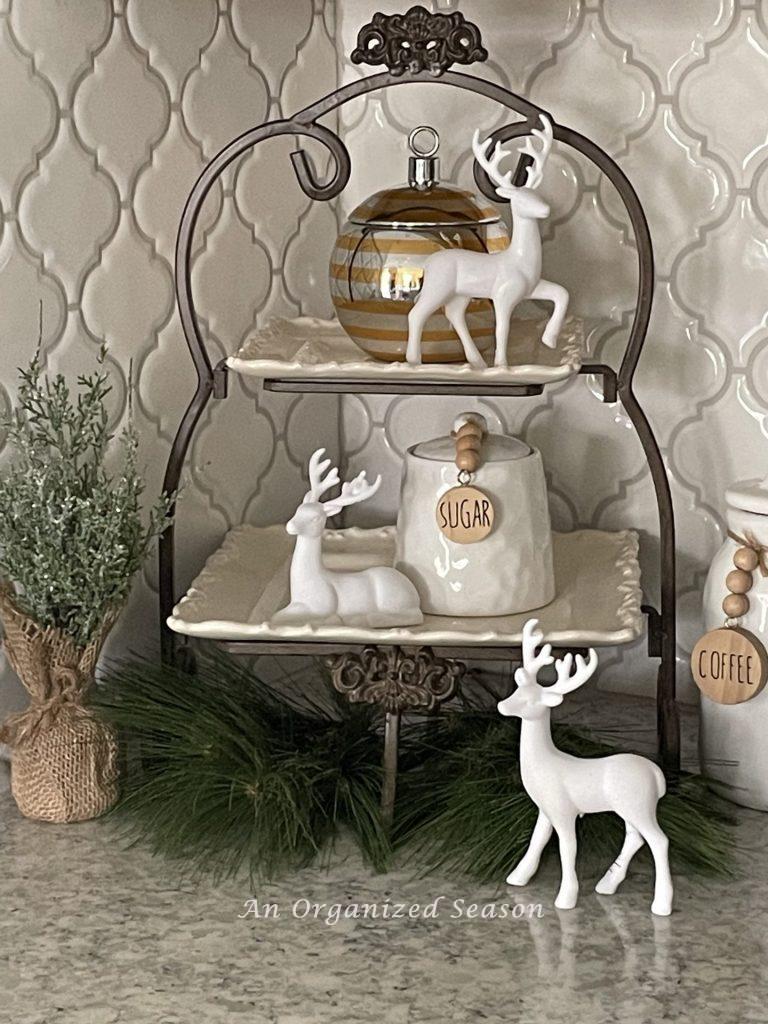 A two tiered tray with white velvet deer and evergreen pieces and a candle. 