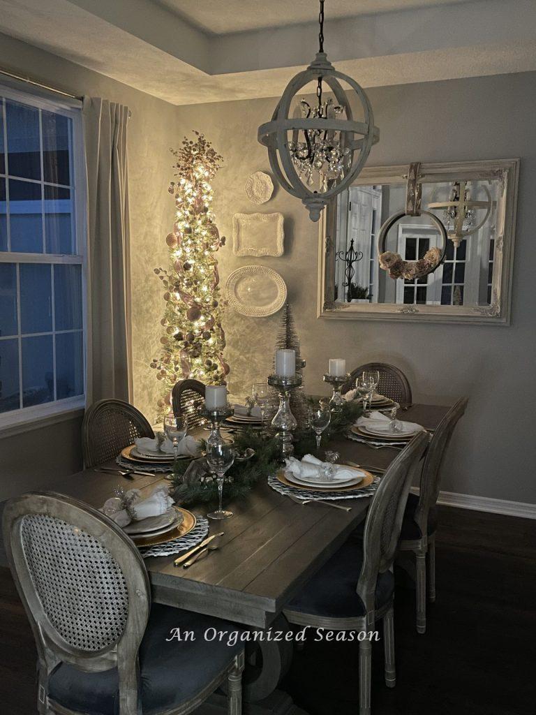 A slim Christmas tree lights a dining room on a nighttime home tour.