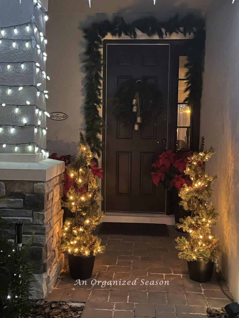 A front porch decorated for Christmas with lights, poinsettias, garland, and a wreath.