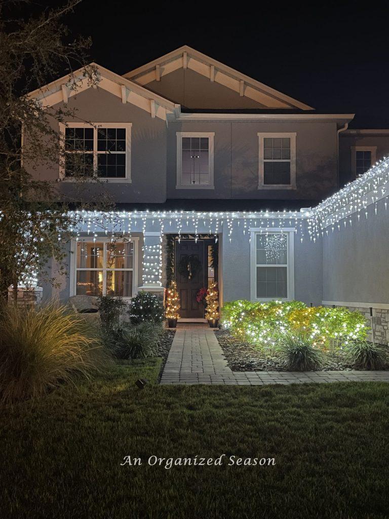 A house with icicle lights and lights on the shrubs. 