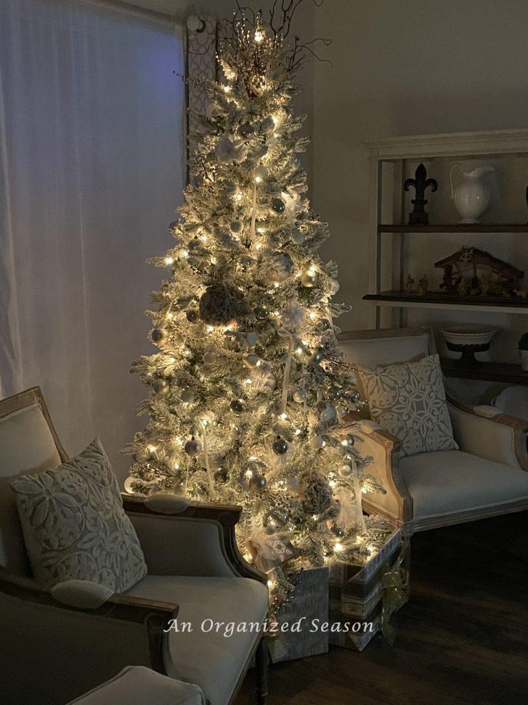 A flocked Christmas tree flanked by two Louis chairs and lit up for the nighttime home tour. 