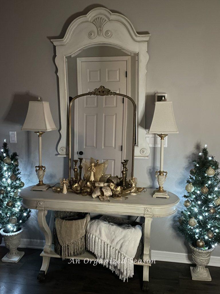 Table and mirror in a foyer with two small Christmas trees with fairy lights on either side of it.