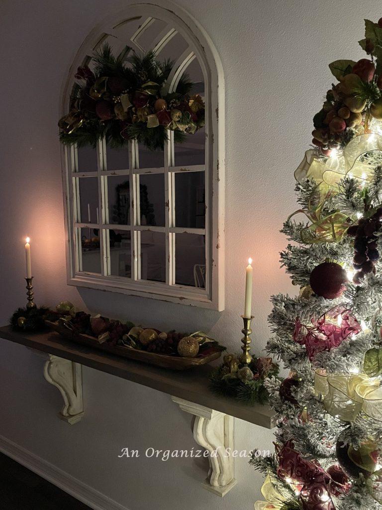 A shelf with a dough bowl full of faux fruit and brass candlesticks that are lit. 