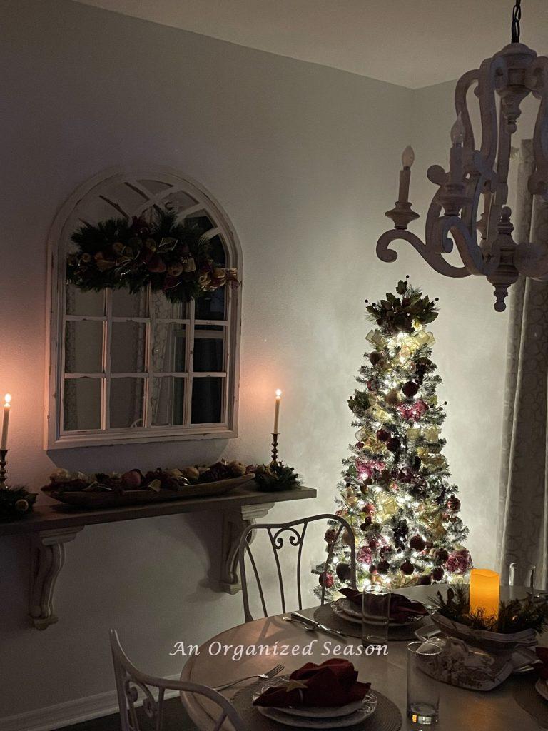 A lit tree tucked in the corner of an eat-in kitchen that's decorated for Christmas. 