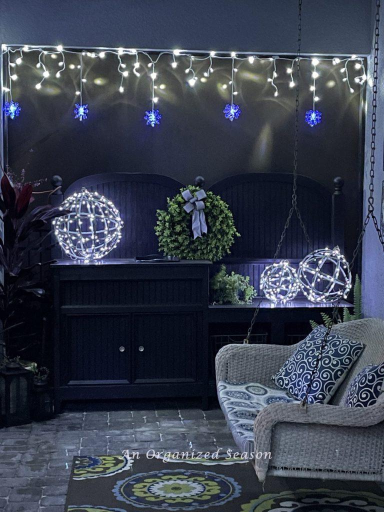 A porch with lighted orbs on a potting bench and icicle lights twinkling above it. 