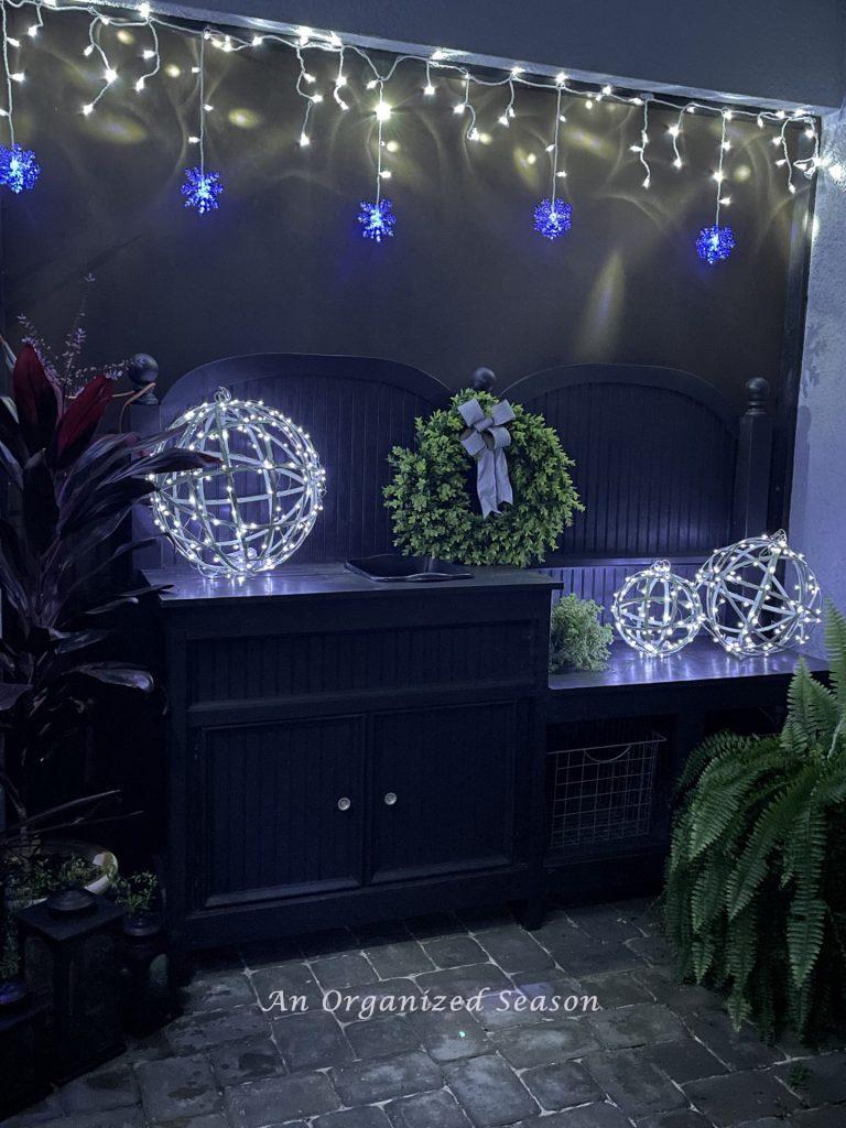 A black potting bench decorated for Christmas with a wreath, and three lighted orbs. 