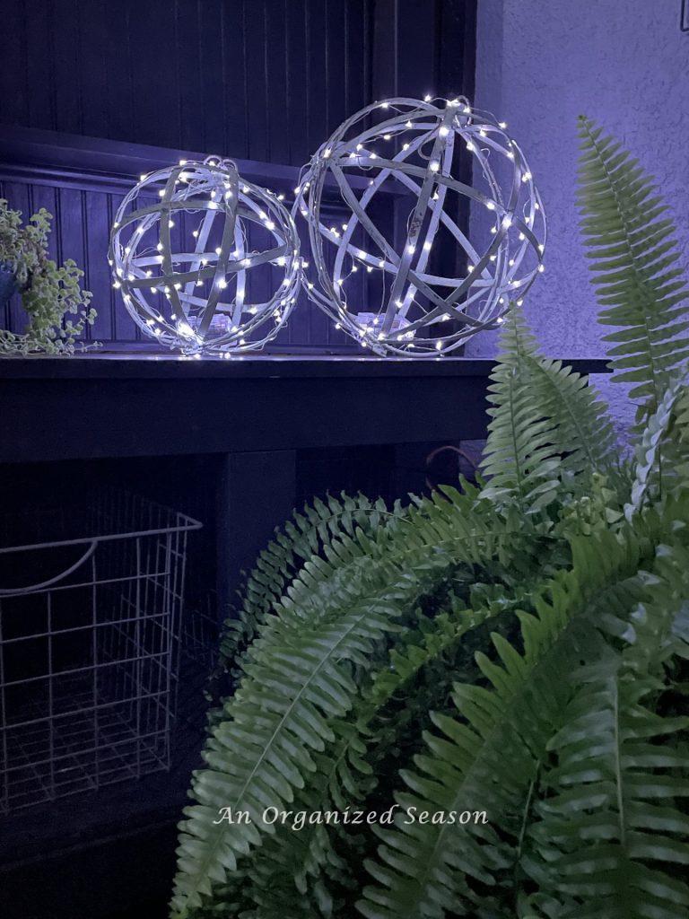 Two metal orbs covered with fairy lights, sitting on a potting bench.  