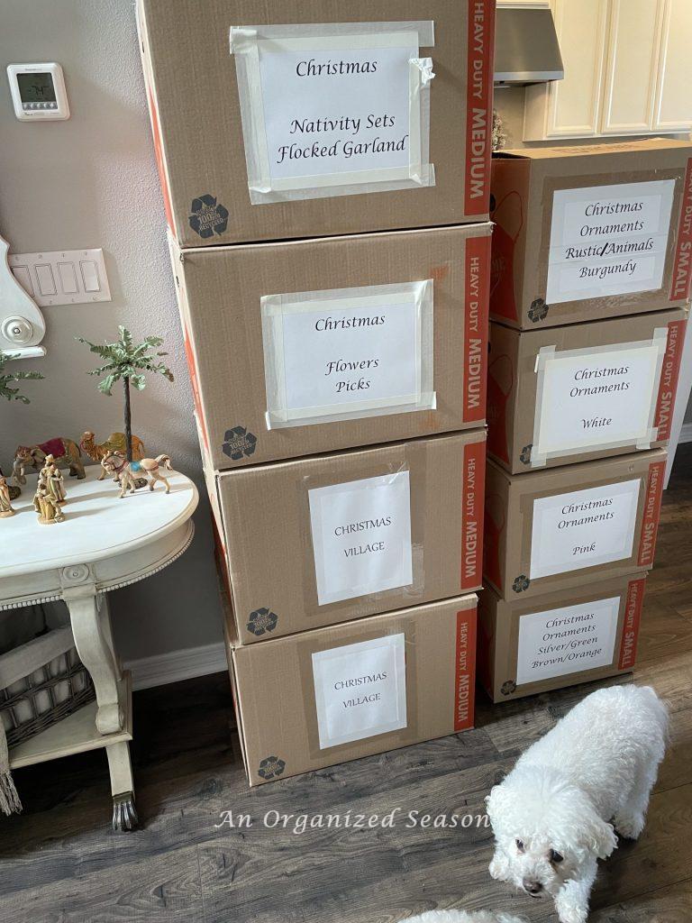 Eight moving boxes stacked up with labels on the fronts showing tips to organize and store your Christmas decor.