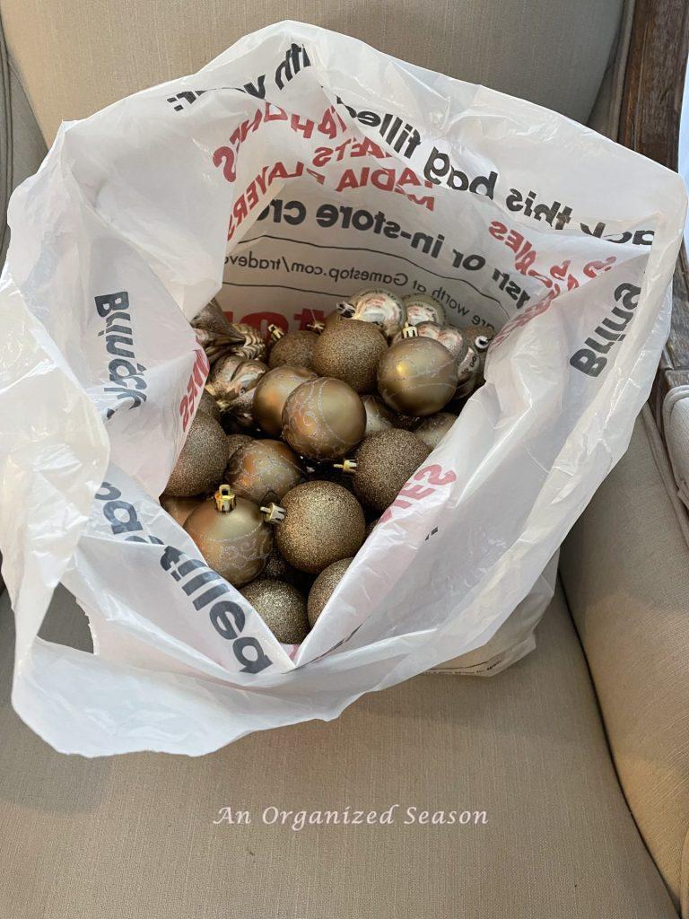 Shatterproof gold ornaments in a plastic shopping bag, showing tips to organize and store your Christmas decor.