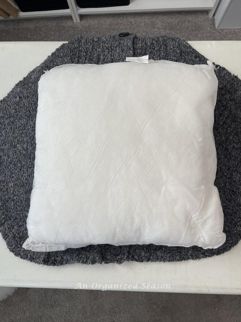 A pillow insert laying on a sweater, step one for how to make cozy home decor with sweaters.