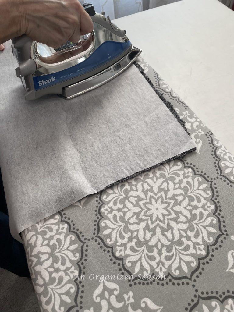 Someone adhering interfacing to a sweater with heat from an iron, step four for how to make cozy home decor with sweaters. 