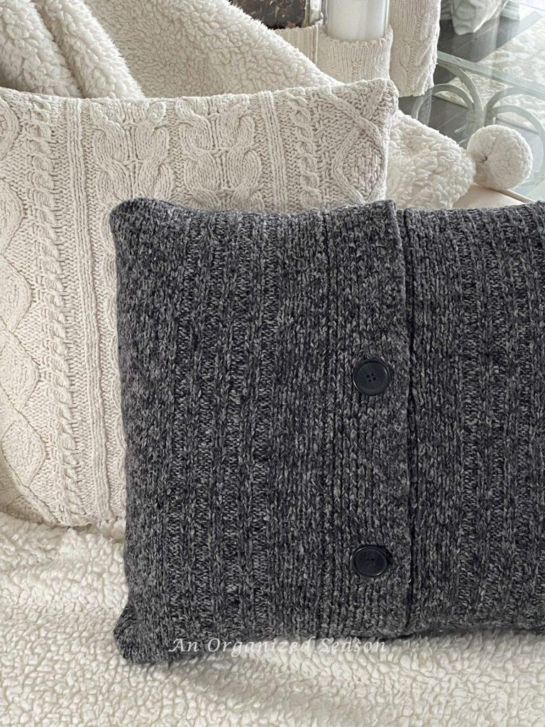 A throw pillow made from a dark grey sweater with black buttons. 