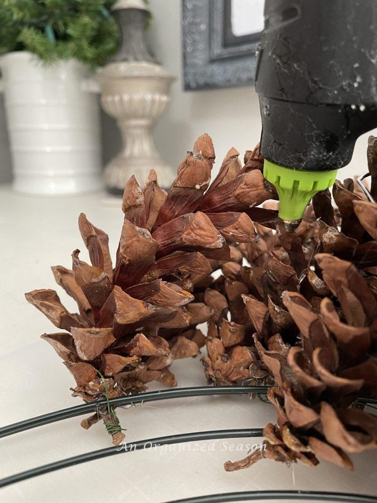 A hot glue gun adhering two pinecones together, step three to make a Winter pinecone wreath.