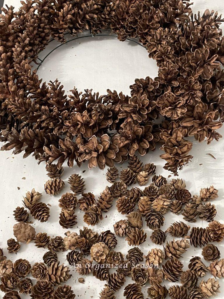 A pinecone wreath surrounded by tiny pinecones scattered on a table.