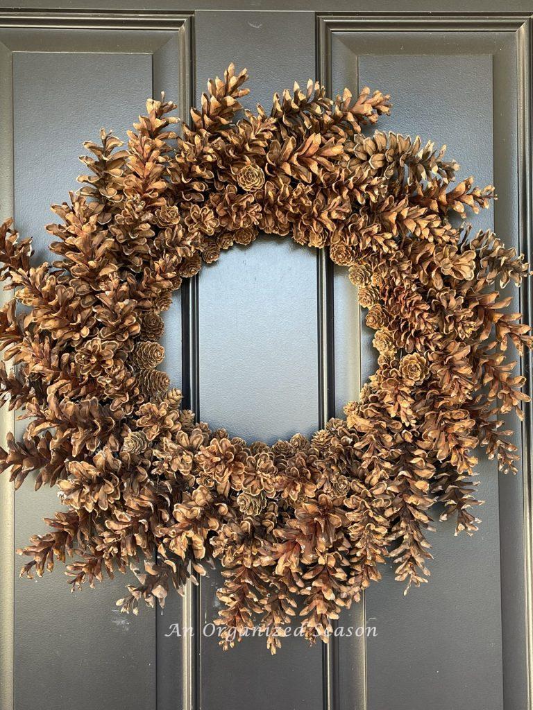 A pinecone wreath hanging on a black front door. 