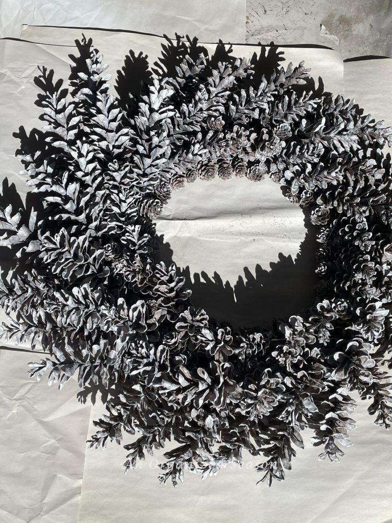 A pinecone wreath with one coat of white spray paint. 