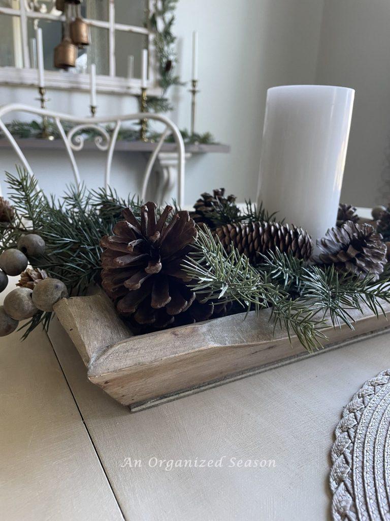 A wood bowl with evergreen, pinecones, and a white candle. 