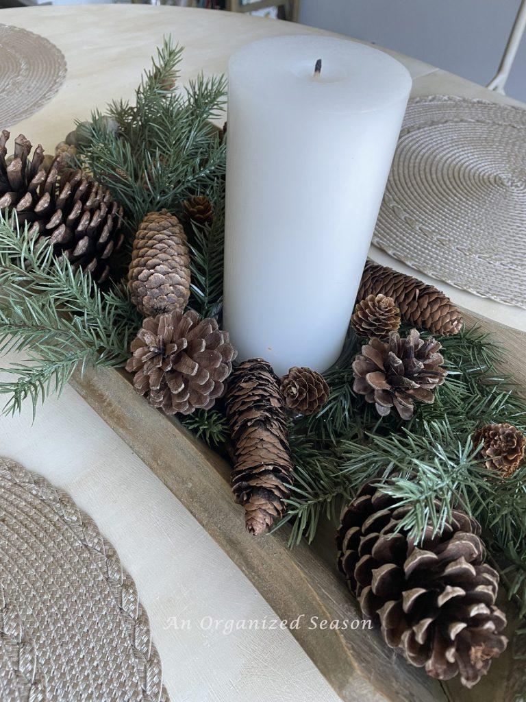 A wood bowl filled with evergreen, pinecones, and a white candle. 