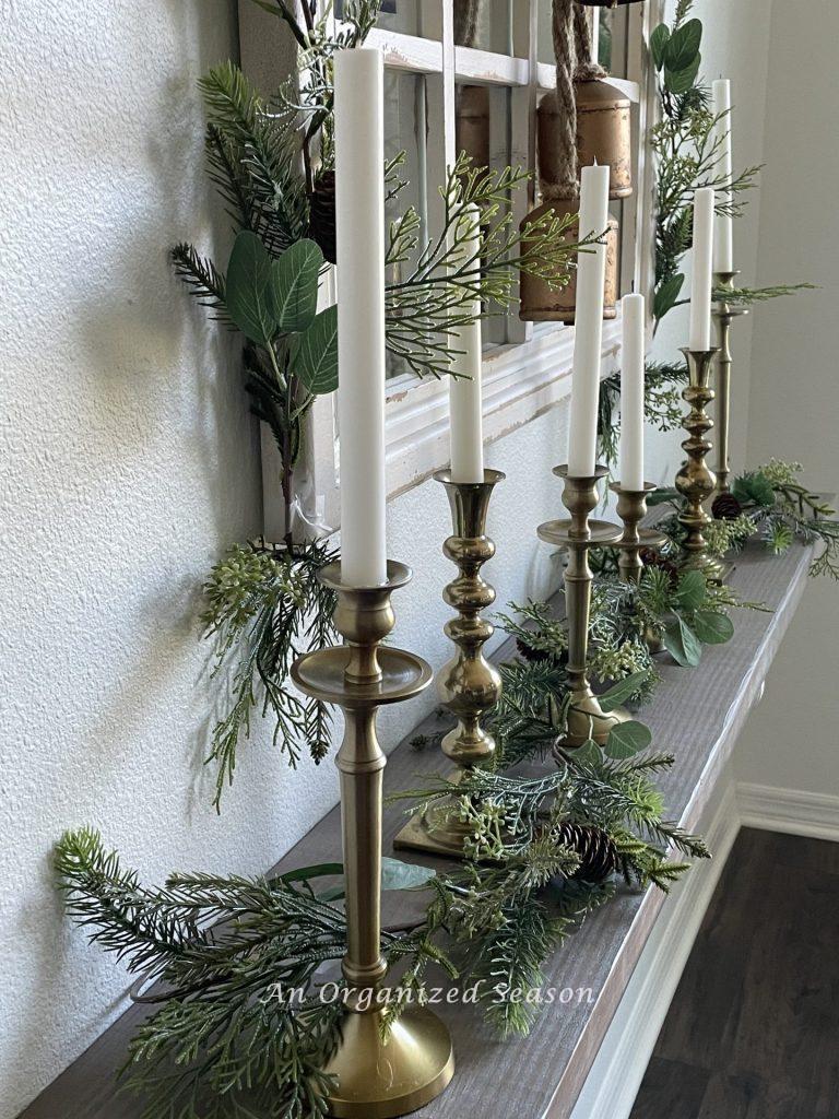 Six brass candlesticks with white taper candles line a shelf,  a perfect example of  Winter decor ideas that don't look like Christmas!