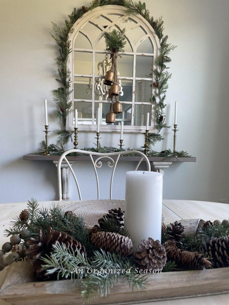 A mirror and shelf decorated with evergreen garland and brass candlesticks and bells. 