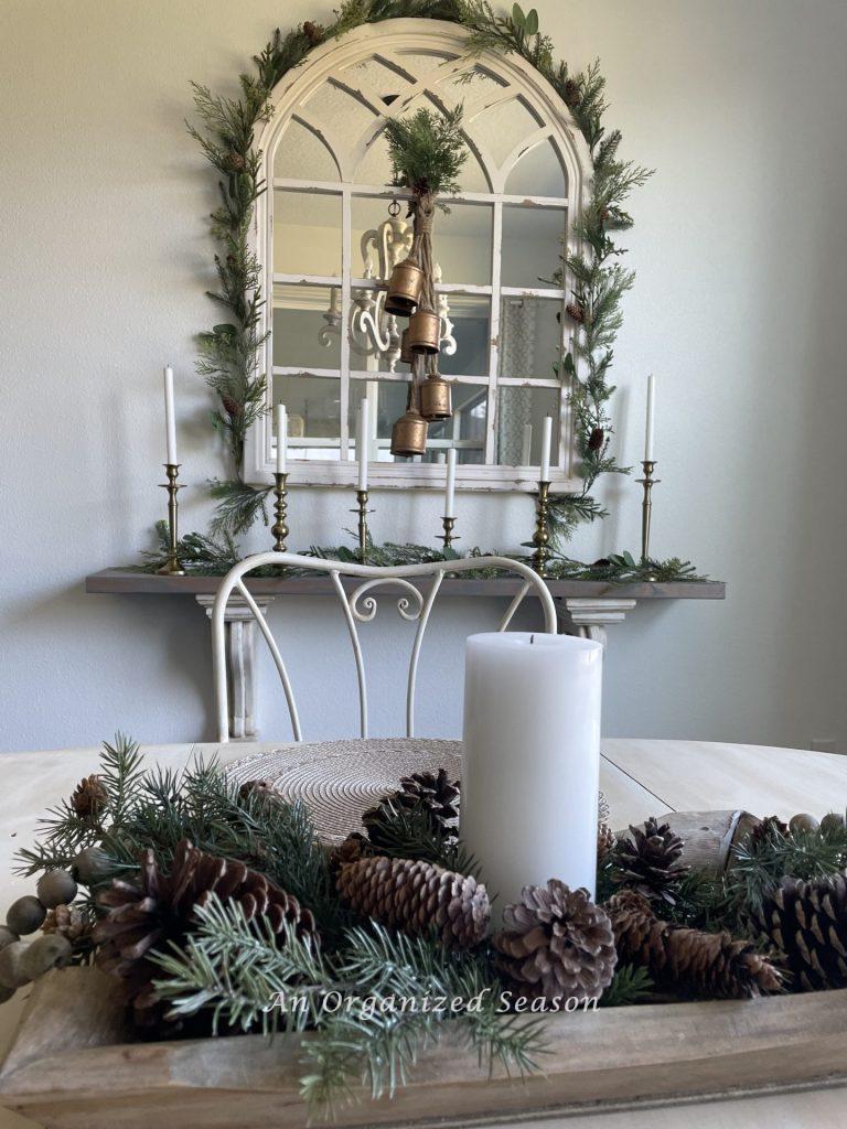 A mirror and shelf decorated with evergreen garland and brass candlesticks and bells.